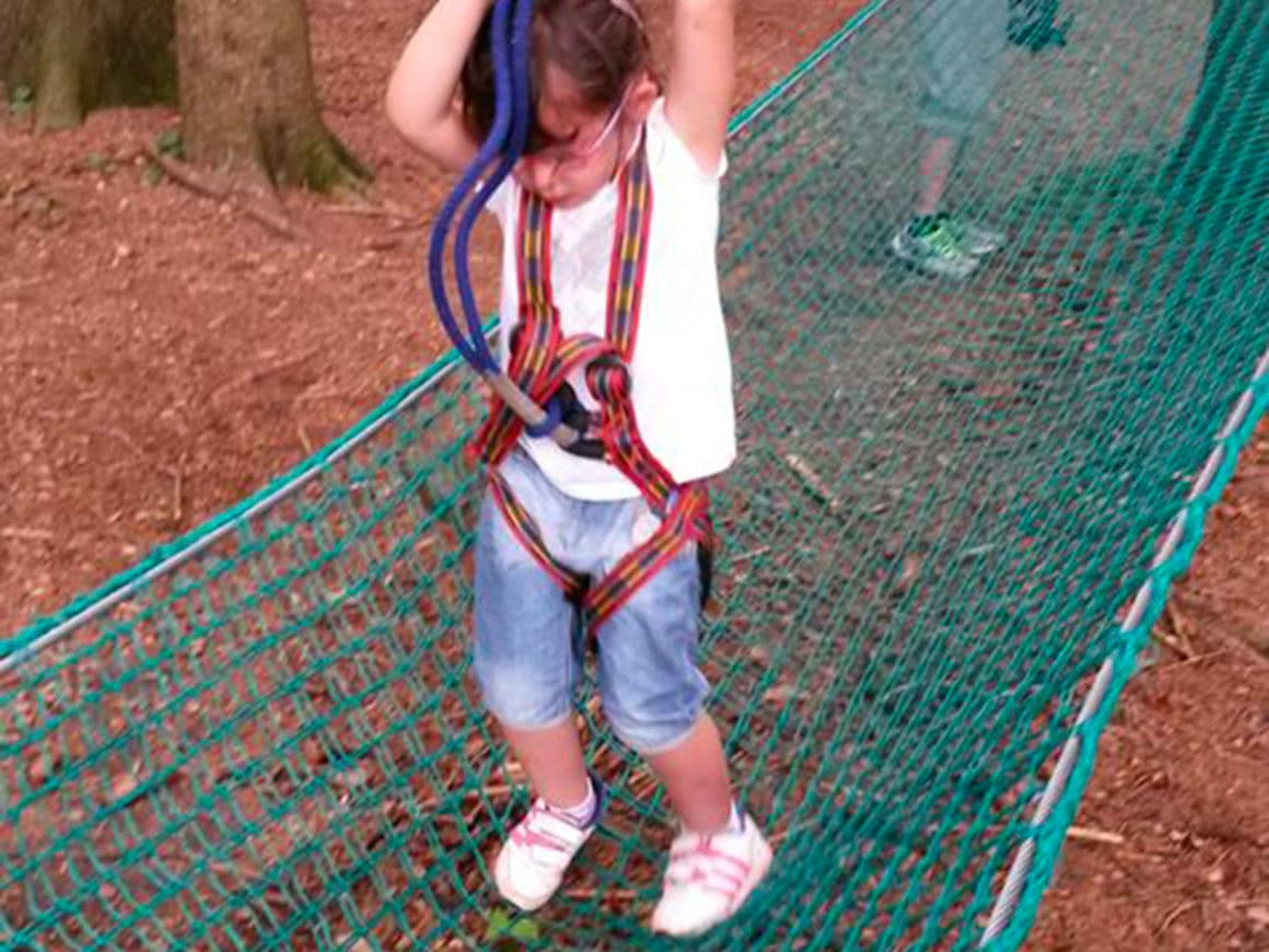 Bambina supera il ponte di rete del percorso Bimbi del parco avventura di Civenna
