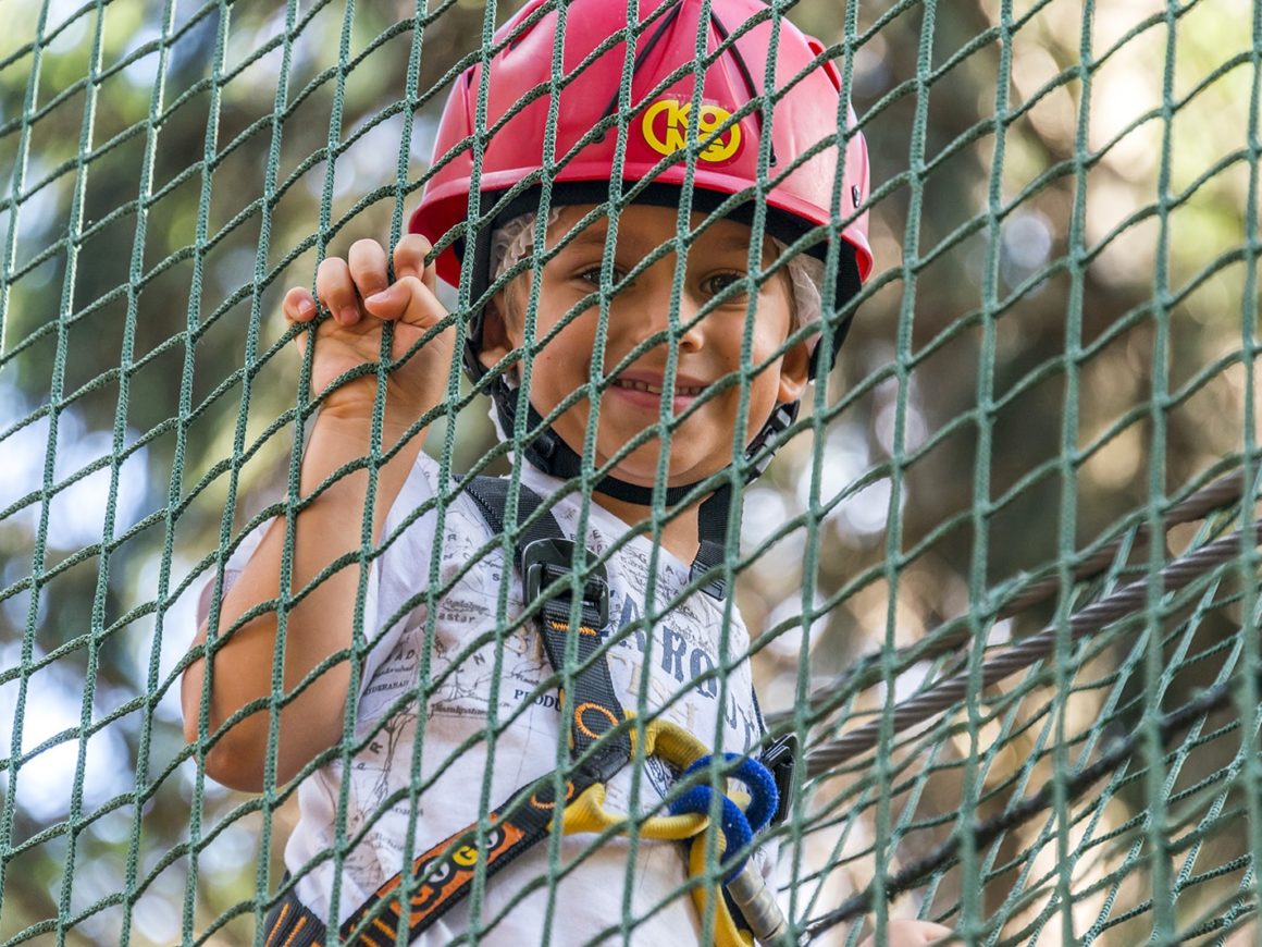 Bambino con caschetto e imbragatura di sicurezza al parco avventura vicino al lago di Como