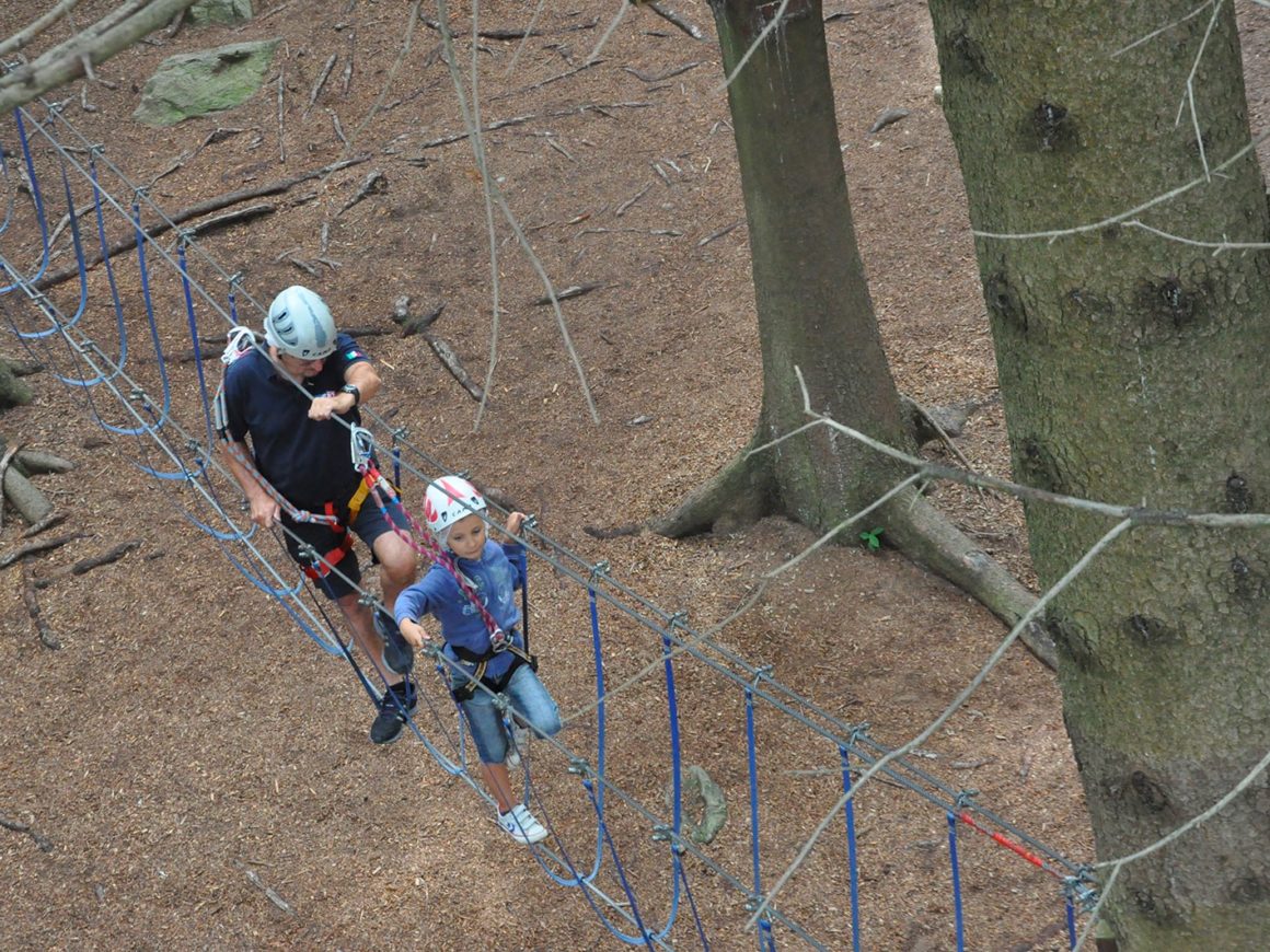 Papà e figlia superano i percorsi tra gli alberi al parco avventura in Lombardia
