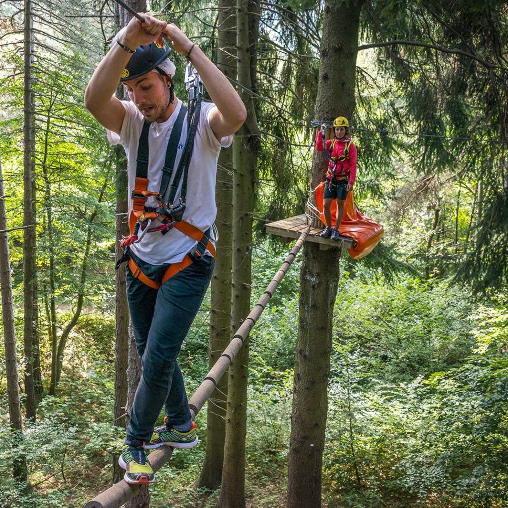 Ragazzo affronta una trave sospesa tra gli alberi nel parco avventura di Civenna