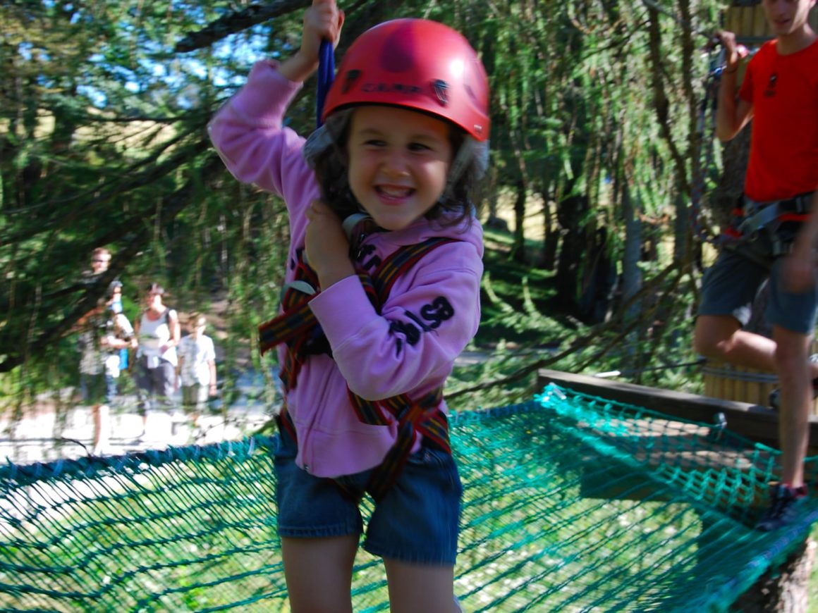 Bambina su un ponte a rete del percorso tra gli alberi nel parco avventura